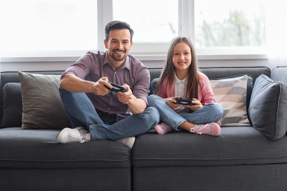 Padre e figlia che giocano insieme ai videogame - Mercato italiano dei videogiochi, crescita del 5% nel 2023. Superati i 2,3 miliardi di euro secondo la ricerca di IIDEA